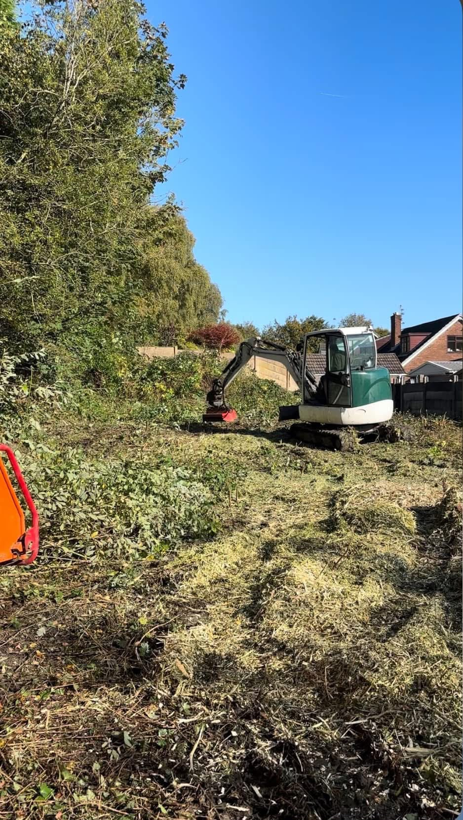 Mini excavator with a mulching head clearing an overgrown plot beside houses